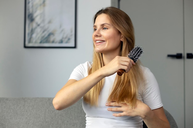 smiling woman brushing her long hair looking away sitting at home. Beauty and hair care concept