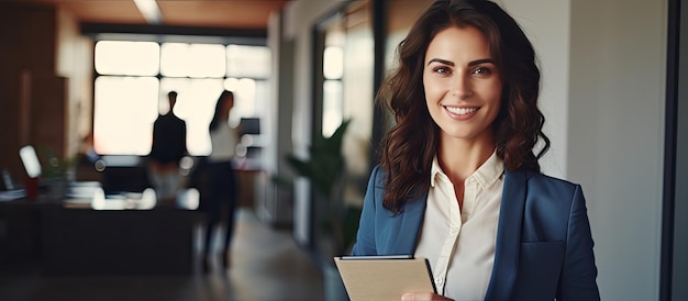 A smiling woman in casual attire holding a pencil and notebook standing in a contemporary office looks at the camera with empty space around her