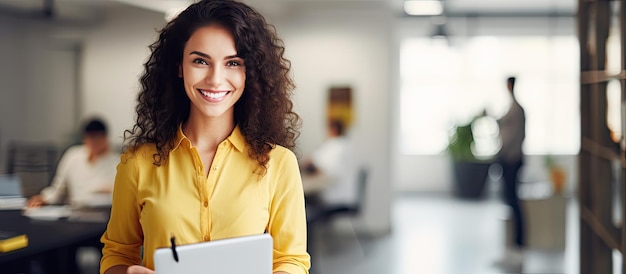 A smiling woman in casual attire holding a pencil and notebook standing in a contemporary office looks at the camera with empty space around her