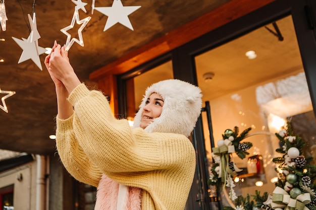 Smiling woman celebrating dressed warm sweater and woolen hat, posing outside