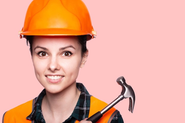 smiling woman in a construction helmet and an orange vest holds a hammer in her hands