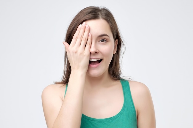 Smiling woman covering an eye with her hand as she stands looking at the camera