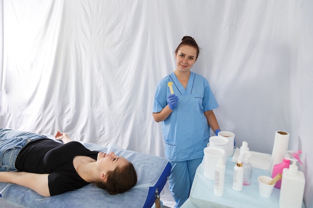 A smiling woman doctor is a beautician next to a woman lying on a massage table