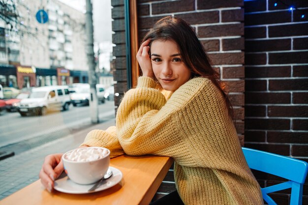 Smiling woman dressed warm sweater, drink marshmallow with milk coffee cacao or latte