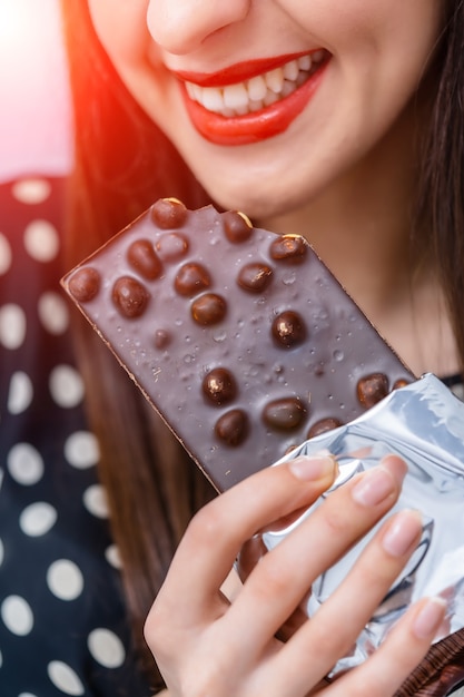 Smiling woman eating chocolate bar with nuts. Sweet life.