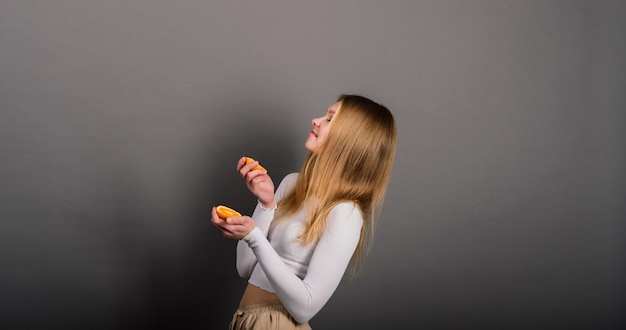 Smiling woman eating orange in studio, half fruit, blonde long hair.