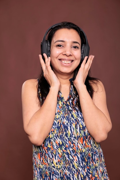 Smiling woman enjoying music in wireless headphones, laughing with satisfied facial expression portrait. Model wearing earphones, listening to song, looking at camera studio medium shot