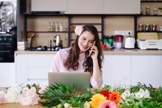 Smiling Woman Florist Small Business Flower Shop Owner She is using her telephone and laptop to take orders for her online store Work from home