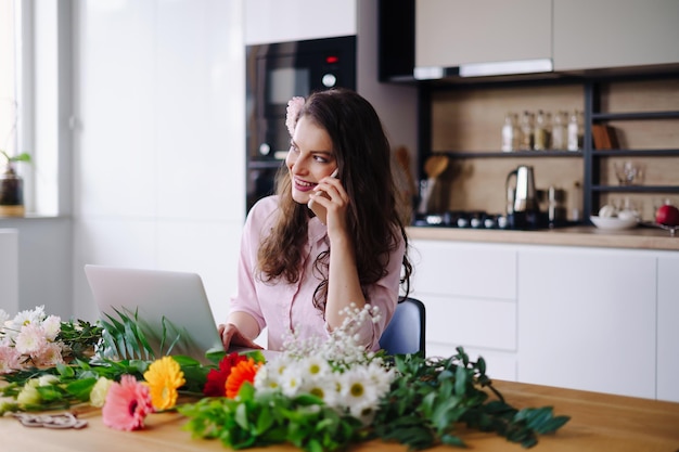 Smiling Woman Florist Small Business Flower Shop Owner She is using her telephone and laptop to take orders for her online store Work from home