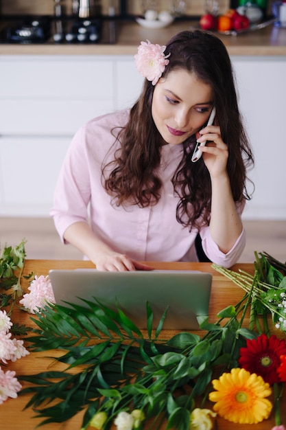 Smiling Woman Florist Small Business Flower Shop Owner She is using her telephone and laptop to take orders for her online store Work from home