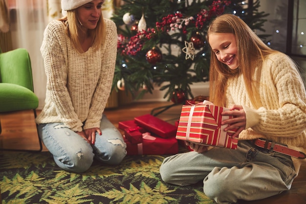 Smiling woman giving present to teenage daughter at Christmas tree