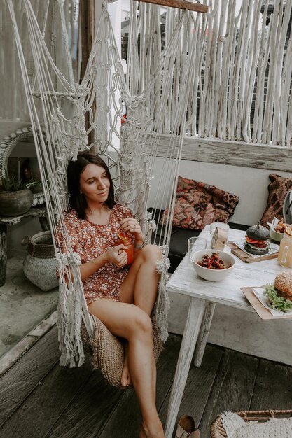 Photo smiling woman having food while sitting on hammock