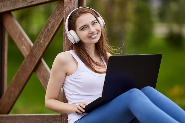 Smiling woman in headphones with laptop outside