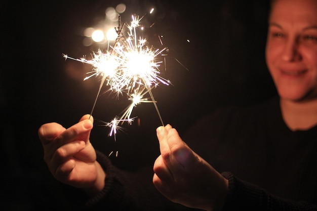 Photo smiling woman holding illuminated sparklers at night