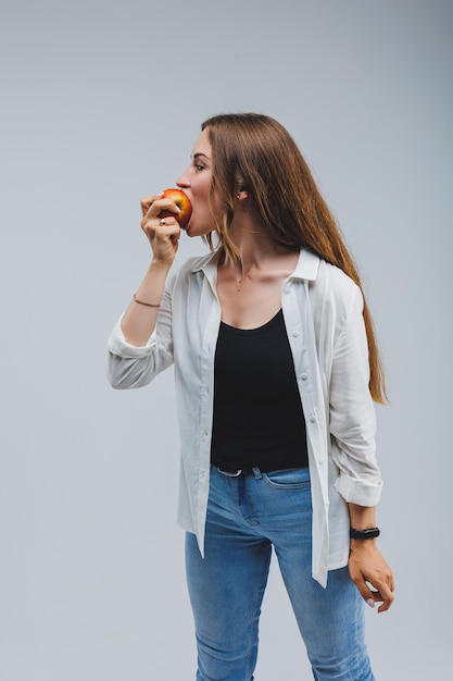 Smiling woman holding a red apple Beautiful brunette in a white shirt Healthy plant food and vitamins White background