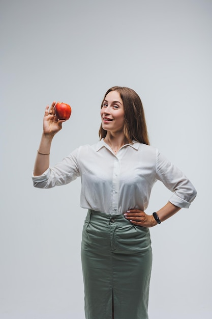 Smiling woman holding a red apple Beautiful brunette in a white shirt Healthy plant food and vitamins White background