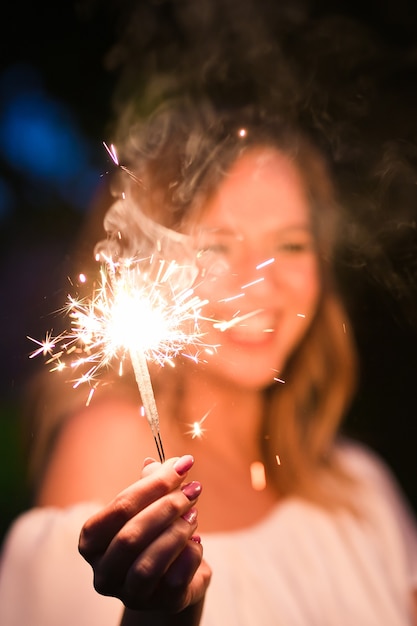 Photo smiling woman holding sparkler and celebrating outdoor