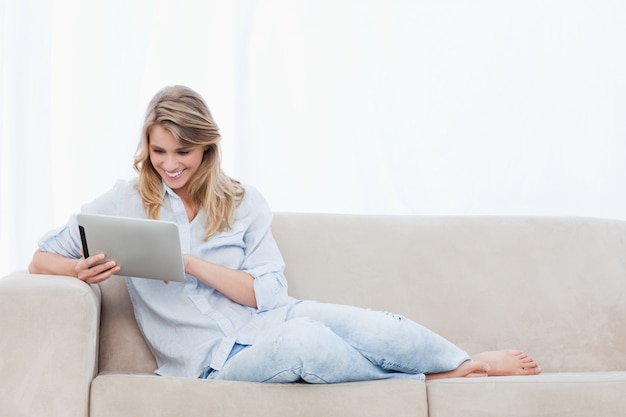 A smiling woman holding a tablet is sitting on a couch