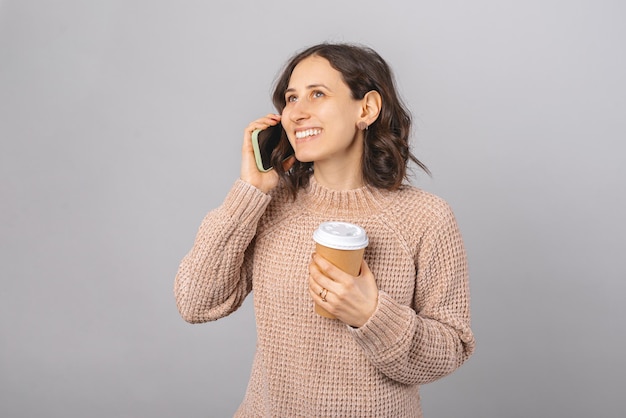 Smiling woman is having a phone call while holding a paper cup