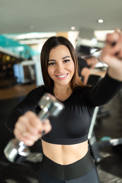 Smiling woman is losing weight and exercising with dumbbells The concept of sports and recreation Beautiful woman in sportswear with dumbbells in her hands