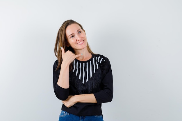 The smiling woman is showing mobile phone gesture with hand on white background