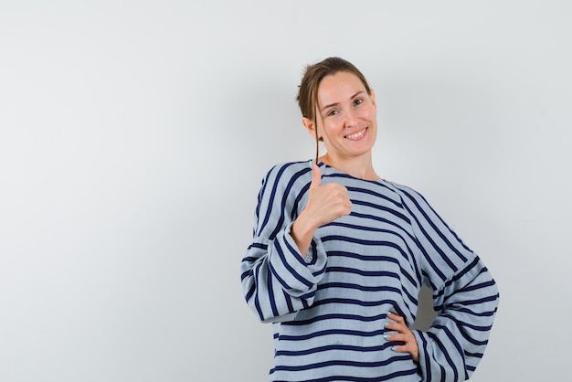 The smiling woman is showing perfect gesture with one hand and putting other on waist on white background