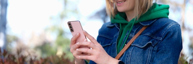 Smiling woman looks at phone on street getting good news in chat concept