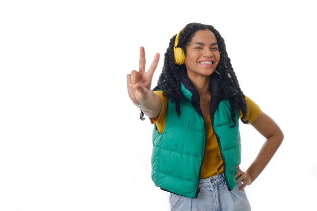 Smiling woman makes peace sign with hand while enjoying listening to music with headphones.