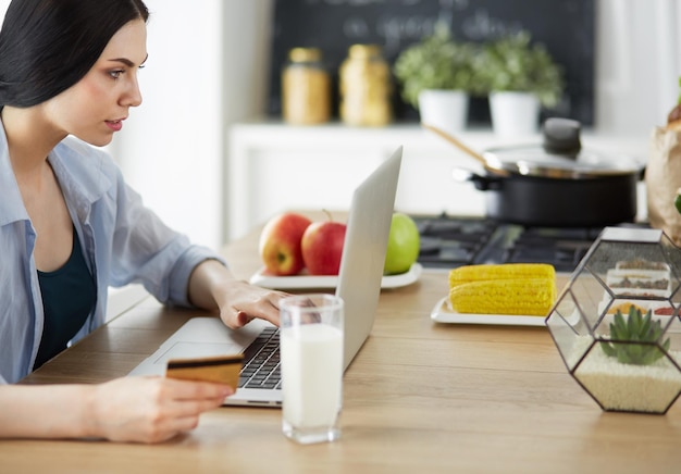 Smiling woman online shopping using computer and credit card in kitchen