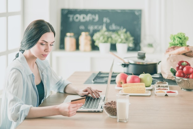 Smiling woman online shopping using computer and credit card in kitchen