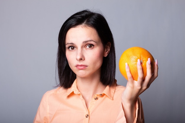 smiling woman in orange shirt holding grapefruit in her hands