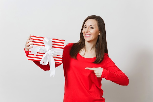 Smiling woman pointing on red striped present box with ribbon isolated on white background. For advertisement. St. Valentine's Day, International Women's Day, Christmas, birthday, holiday concept.