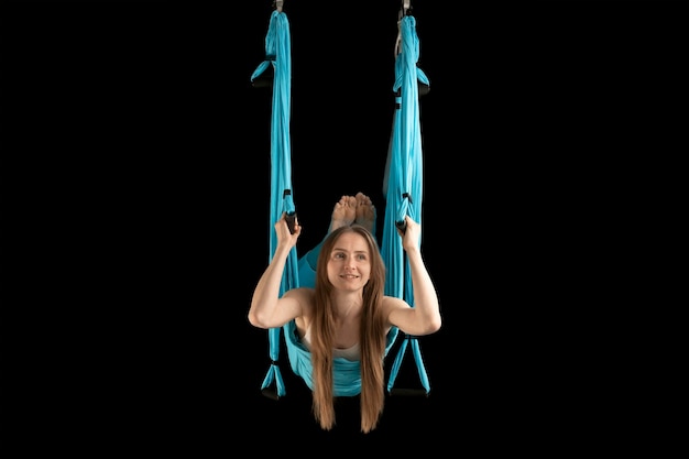 Smiling woman practicing Fly yoga Intense gymnast training in sports hammock Aerial gymnastics Black background