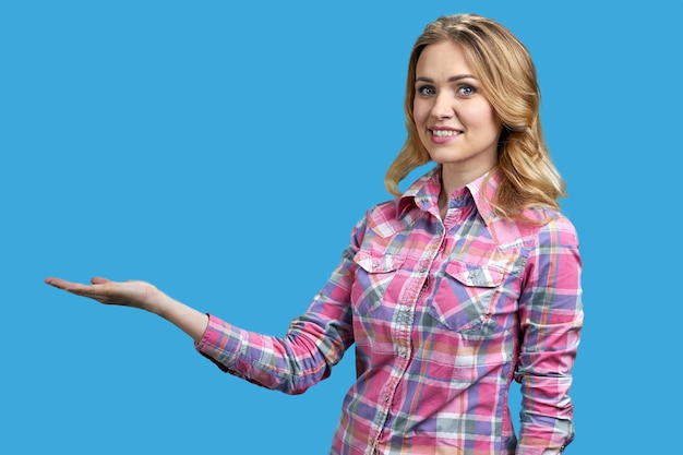 Smiling woman presenting something with open hand palm on blue background