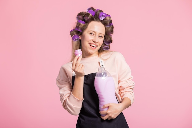 Smiling woman promotes laundry detergent on pink studio background sniffs fabric softener with beautiful pleasant fragrance ad space