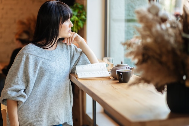 Smiling woman reading book at coffee shop. Picture of young pretty woman sitting at the table in cafe and reading book.