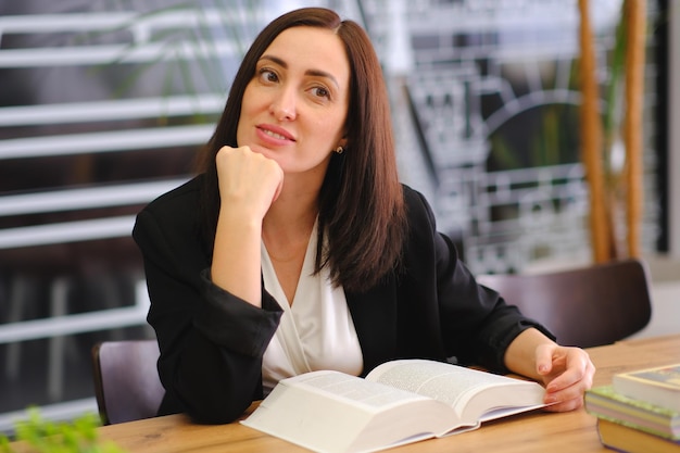 Smiling woman reading book in a library for education studying learning and research at school