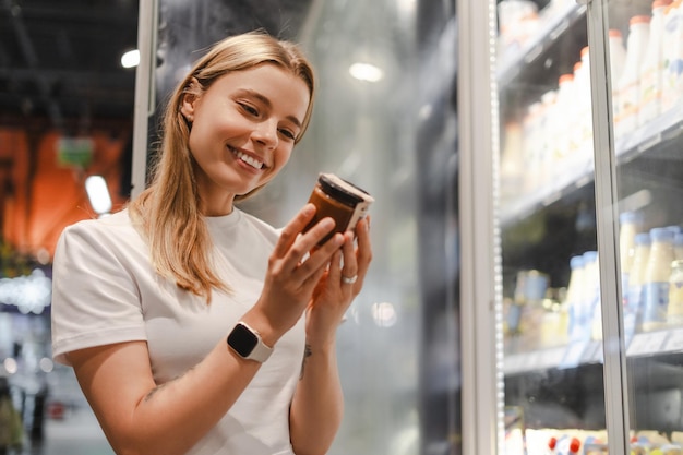 Smiling woman reading product information while shopping in supermarket