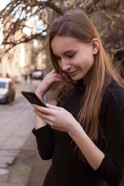 Smiling woman reading text message on smart phone at the street