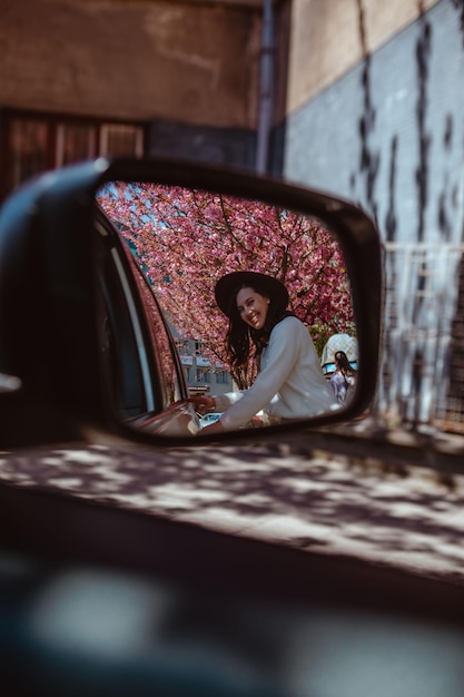 Smiling woman reflection in car rear mirror blooming sakura tree on background