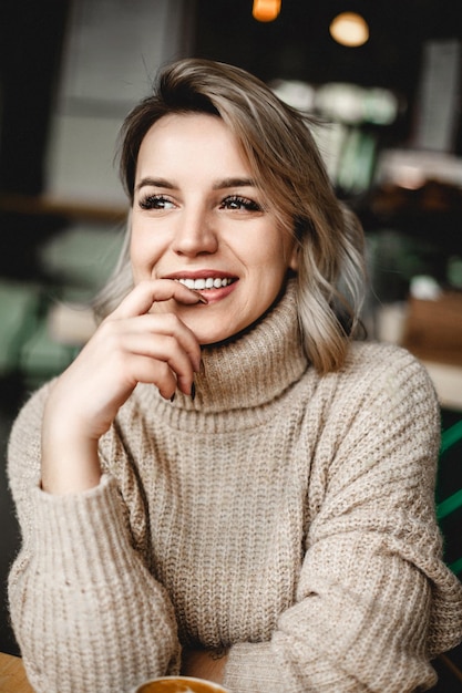 Smiling Woman Relaxing at Table Relaxed woman in sweater sits at table smiling with hands on chin