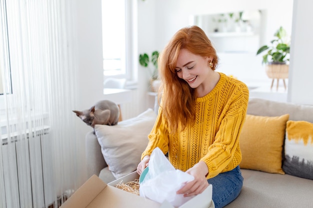 Smiling woman sit on couch at home open post package shopping online buying goods on internet happy young female customer unpack postal shipping parcel satisfied with order or delivery