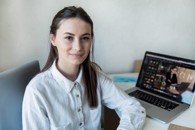 Smiling woman sitting at her desk in office. Happy business woman sitting in office with fingers touching her chin.