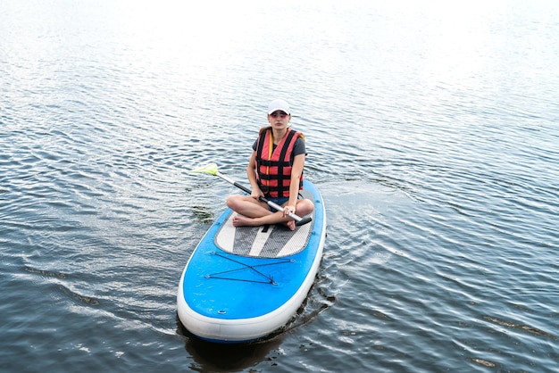 Smiling woman sitting on sup board with paddle