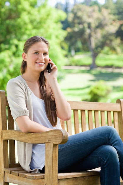 Smiling woman sitting with her mobile phone on a park bench