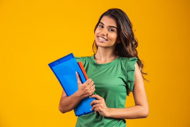 Smiling woman student with school books in hands on yellow background.