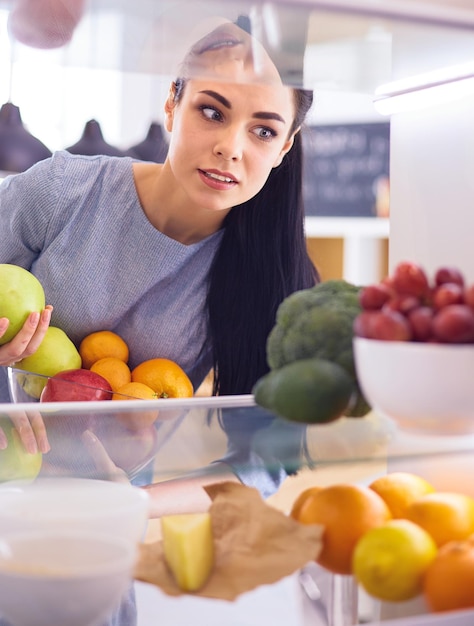 Smiling woman taking a fresh fruit out of the fridge healthy food concept