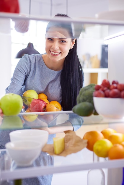 Smiling woman taking a fresh fruit out of the fridge healthy food concept