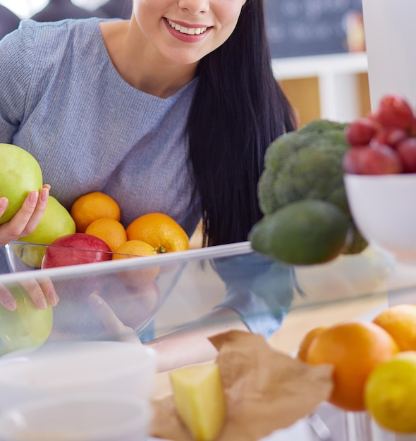 Smiling woman taking a fresh fruit out of the fridge healthy food concept