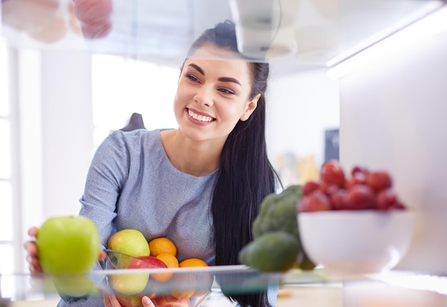 Smiling woman taking a fresh fruit out of the fridge healthy food concept